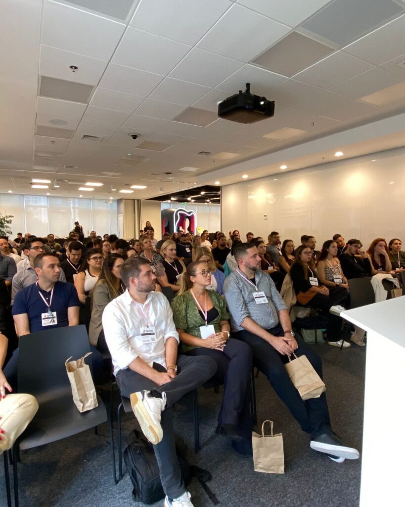 Participantes engajados em uma sessão durante um evento de Team Building Ágil da Electrolux, com foco em agilidade, colaboração e alinhamento de equipes. Os participantes estão sentados atentamente enquanto um palestrante se apresenta à frente da sala. 