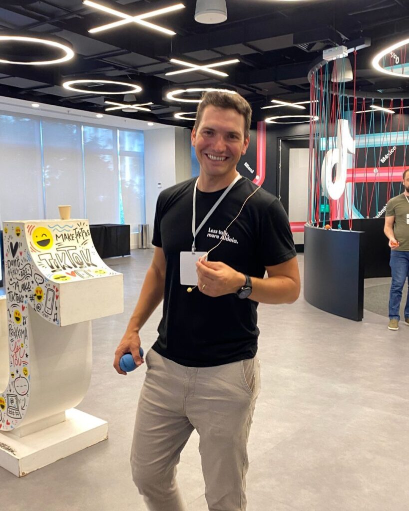Um facilitador sorridente no evento Team Building Ágil da Electrolux, segurando uma bola de malabares, objeto usado durante o Team Building. O evento enfatiza a criatividade e o engajamento da equipe por meio de atividades como malabares.