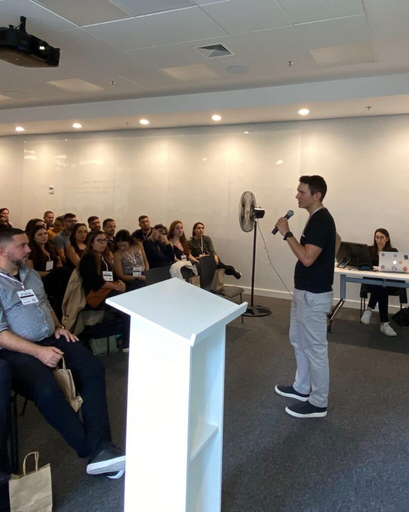 Um facilitador realizando o Team Building Ágil da Electrolux, promovendo a comunicação e a colaboração. Os participantes estão ouvindo atentamente de seus assentos.
