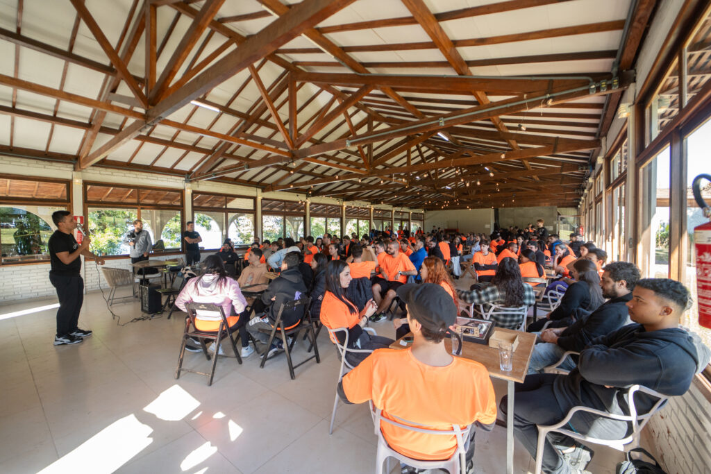 Vista ampla da sala com dezenas de colaboradores engajados na montagem de quebra-cabeças, promovendo colaboração no ambiente de trabalho.