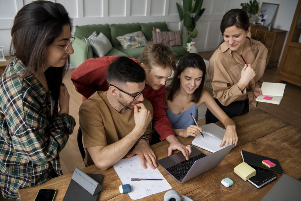 quipe participando de uma atividade de Team Building Corporativo, reunida em torno de um laptop para colaborar e trocar ideias.