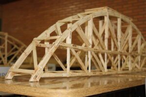 Estrutura de ponte feita com palitos de madeira durante o Workshop Construindo Pontes, representando colaboração e trabalho em equipe