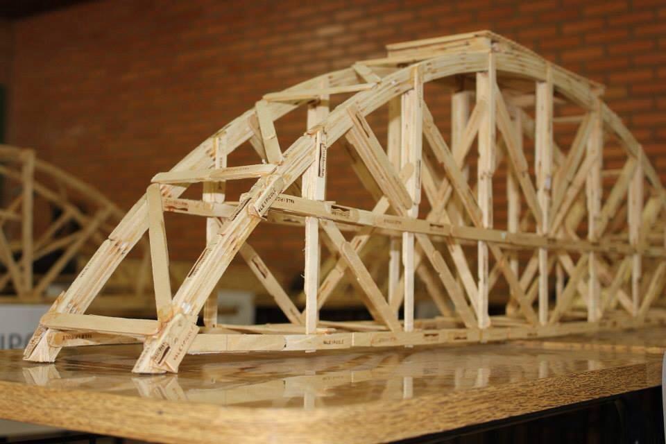 Estrutura de ponte feita com palitos de madeira durante o Workshop Construindo Pontes, representando colaboração e trabalho em equipe